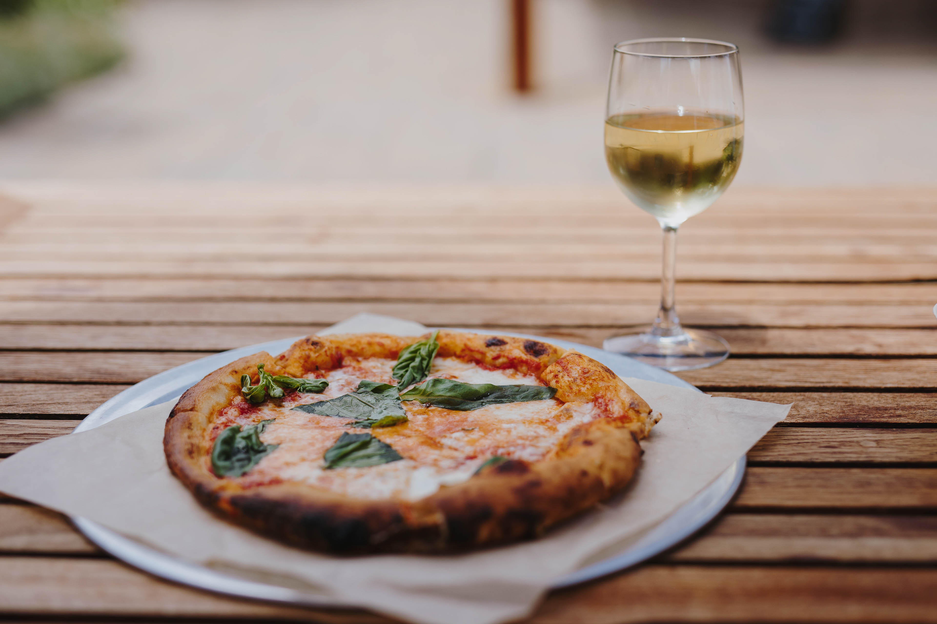 A Margherita Pizza And A Glass Of White Wine On An Outdoor Table